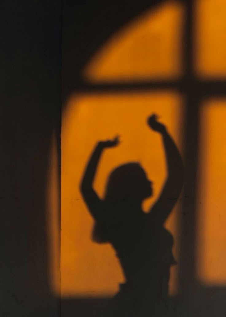 the shadow of a woman standing in front of a window with her arms raised up