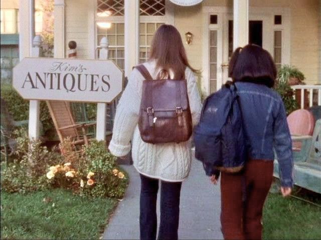 two people are walking down the sidewalk towards an antique store with a clock on it