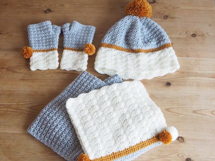 three crocheted hats and two matching mittens on a wooden table with wood flooring