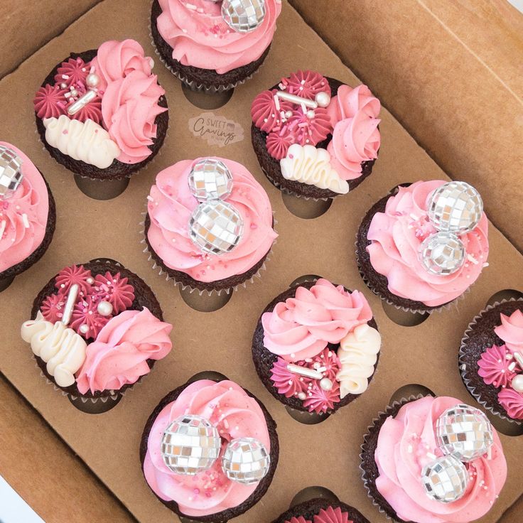 a box filled with lots of pink cupcakes covered in frosting and decorations