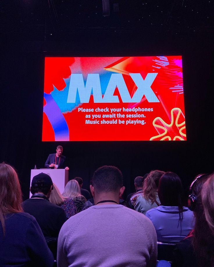 a group of people sitting in front of a large screen with the words max on it