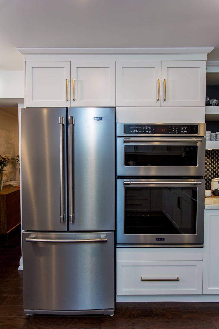 a stainless steel refrigerator and oven in a kitchen with white cabinets, wood flooring and wooden floors