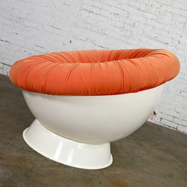 an orange and white chair sitting on top of a cement floor next to a brick wall