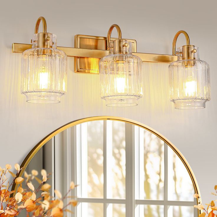 a bathroom vanity with three lights and a mirror on the wall next to flowers in vases