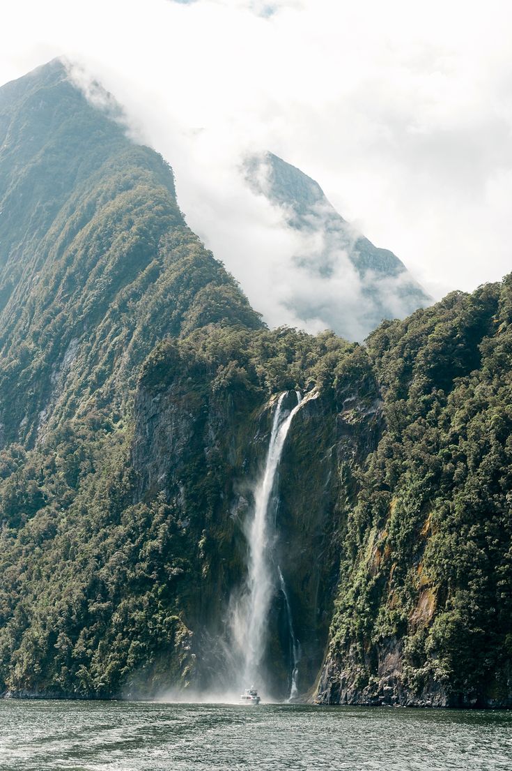 a large waterfall in the middle of a body of water surrounded by mountains and trees