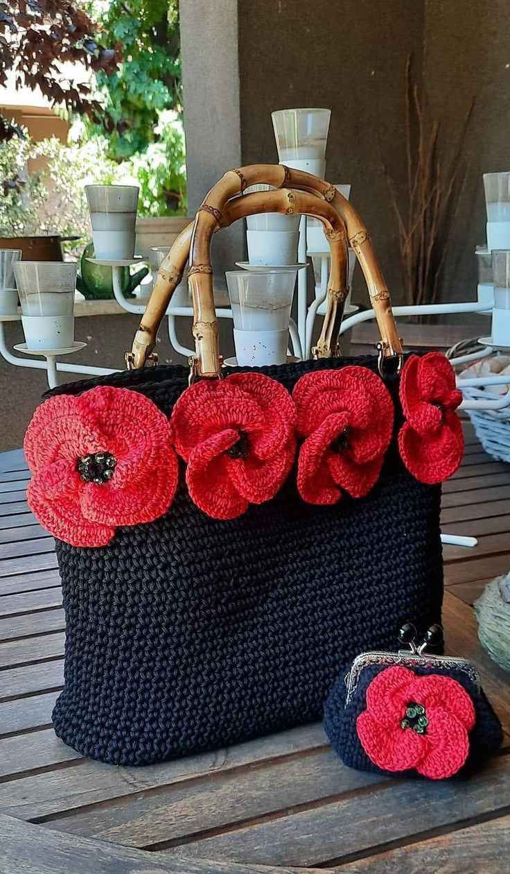 a black purse with red flowers sitting on top of a wooden table next to a straw bag