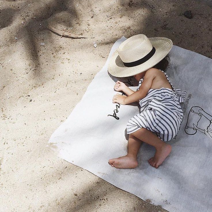 a little boy sitting on top of a towel next to a beach ball and hat