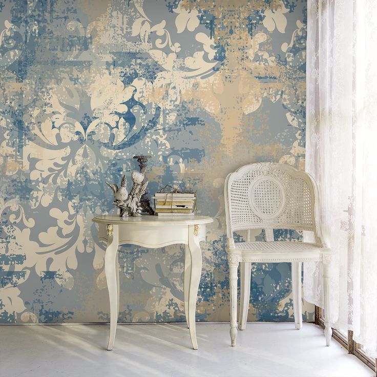 two white chairs and a table in front of a wall with blue flowers on it