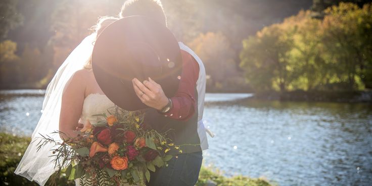 a bride and groom kissing in front of a lake at their wedding day with the sun shining on them