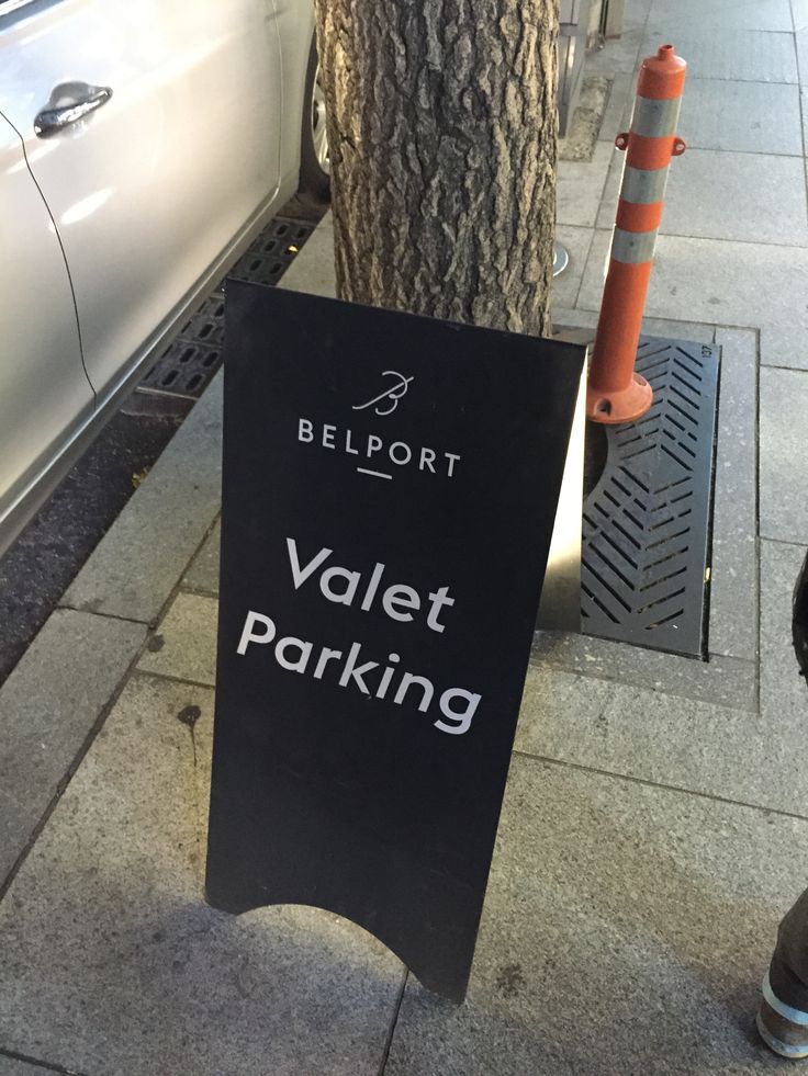 a black sign that says valet parking next to a tree on the side walk