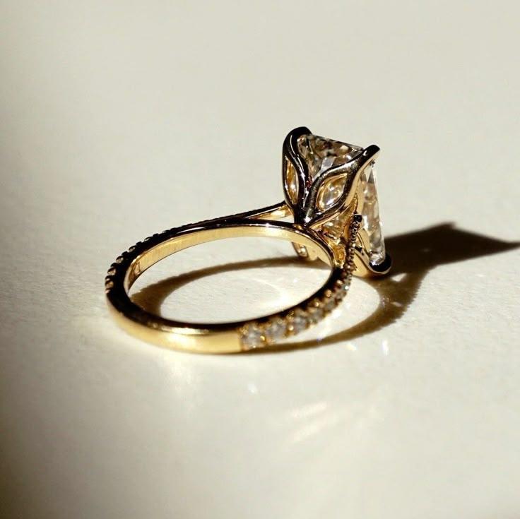 an engagement ring with a fancy diamond set on the front and side, sitting on a white surface