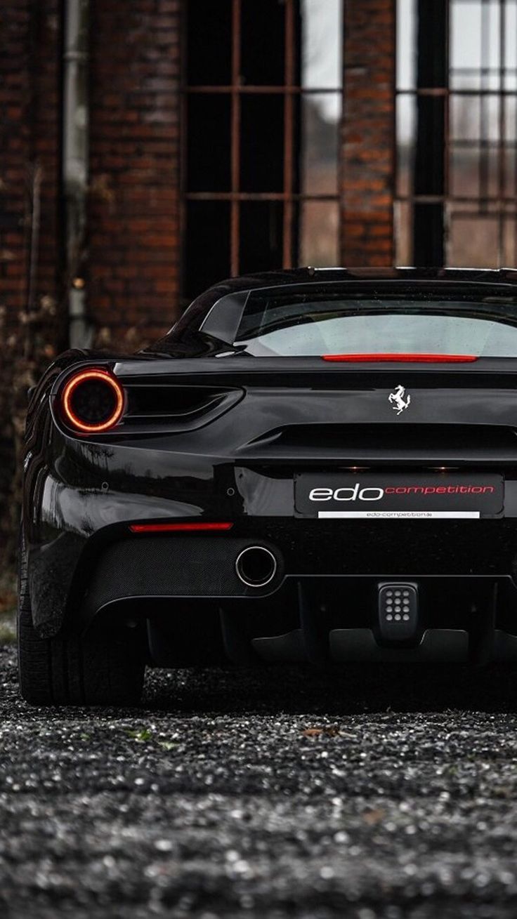 the rear end of a black sports car parked in front of an old brick building