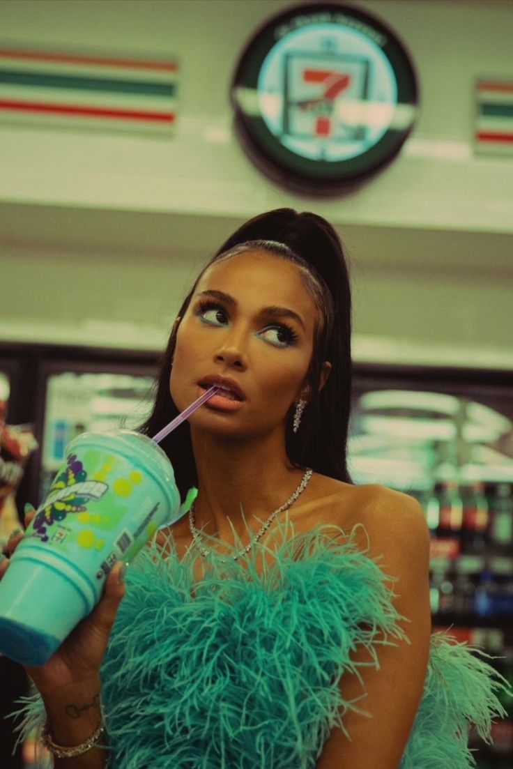 a woman in a feathery dress drinking from a blue drink cup with a straw