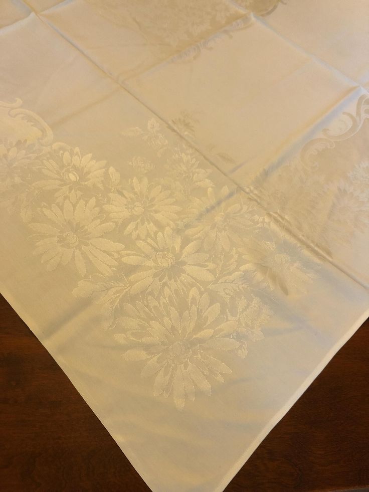 a white table cloth with flowers on it and a wooden table in front of it