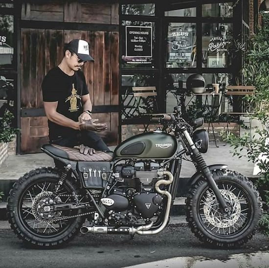 a man sitting on top of a motorcycle parked in front of a building next to trees