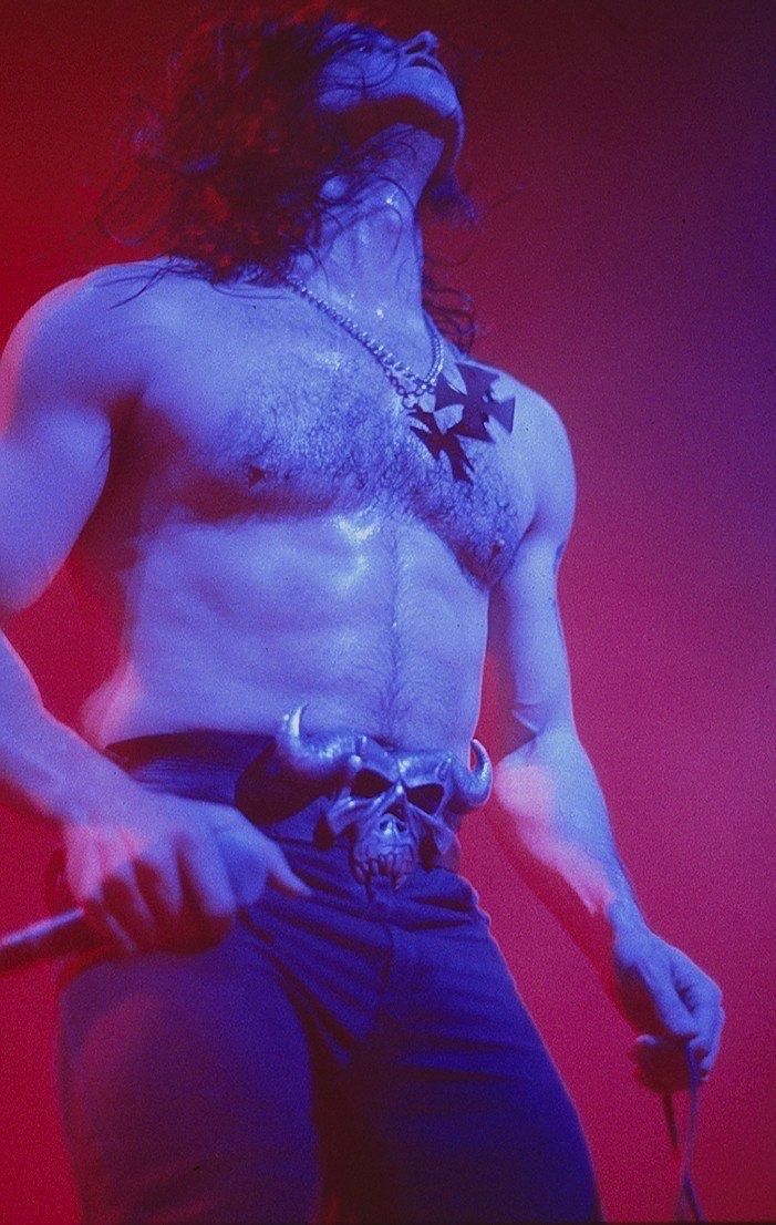 a man with long hair and no shirt on holding a microphone in his right hand