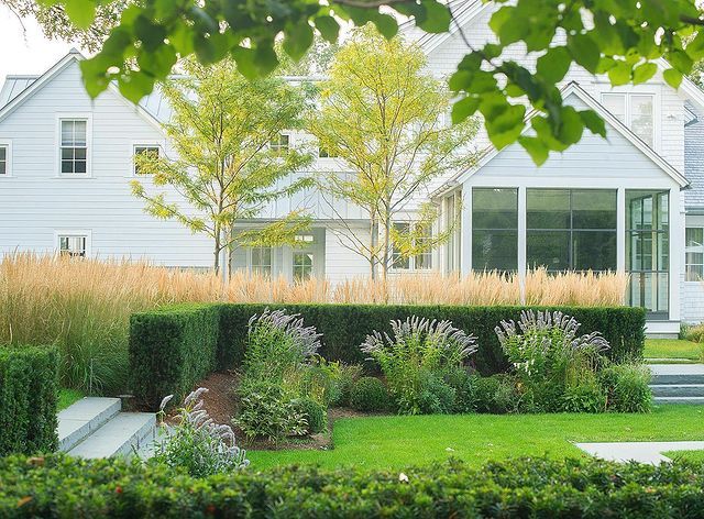 a large white house sitting next to a lush green field with lots of trees and bushes