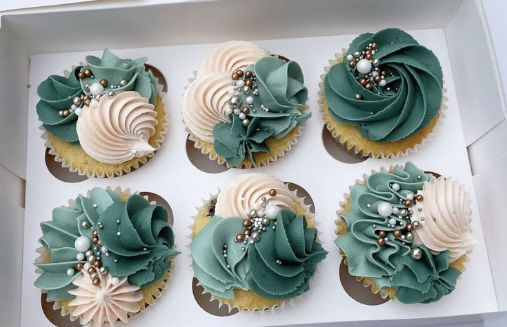 six cupcakes in a box with green frosting and pearls on them, decorated with seashells