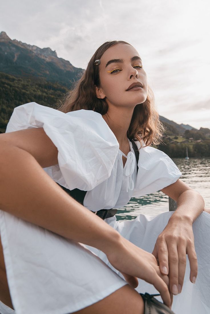 a woman sitting on top of a boat in the water wearing a white shirt and shorts