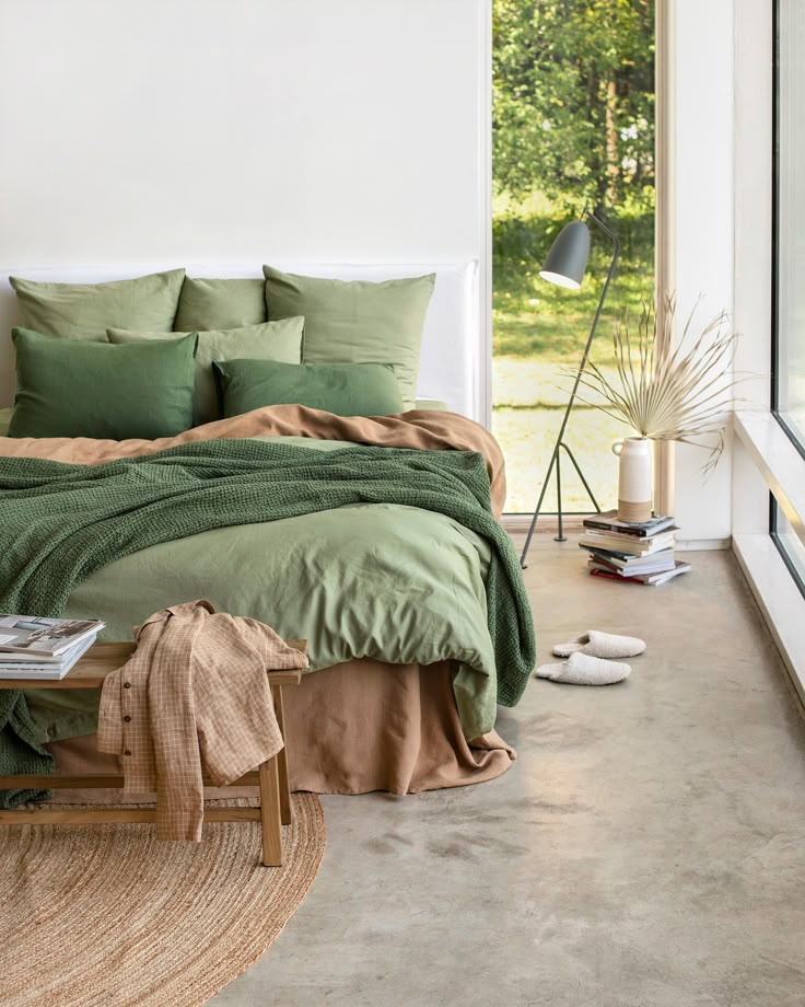 a bed with green sheets and pillows in a room next to a large open window