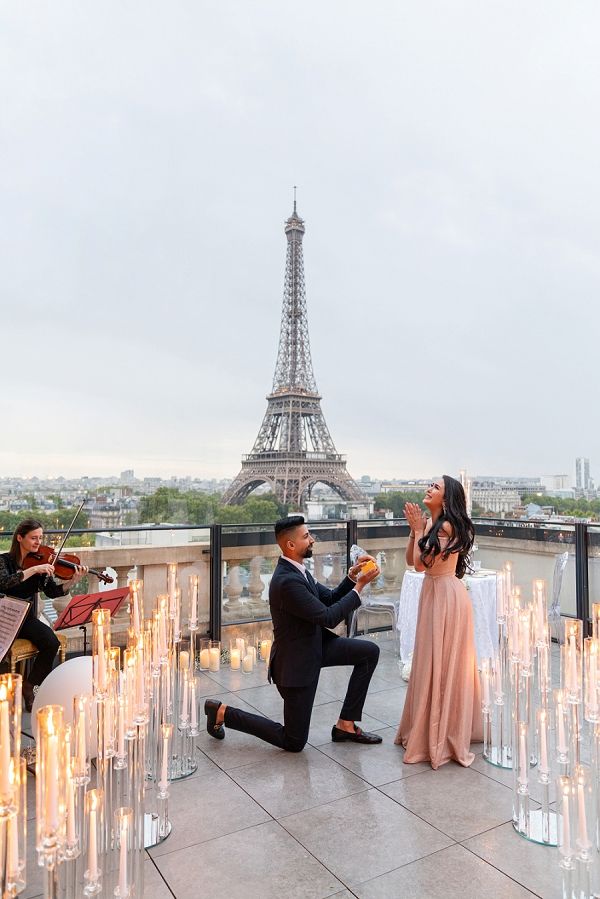 a man kneeling down next to a woman in front of the eiffel tower