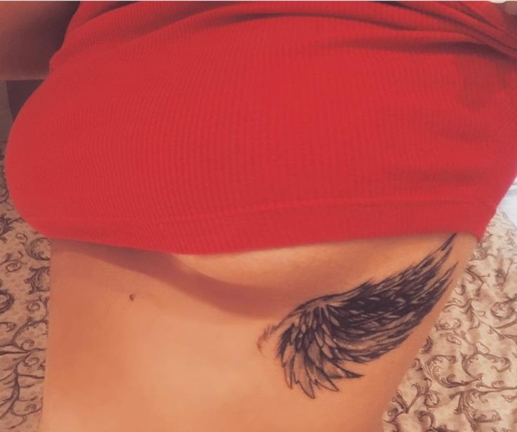 a woman's stomach with a black feather tattoo on it