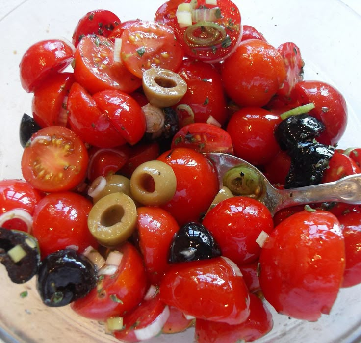 a bowl filled with tomatoes and olives on top of a table