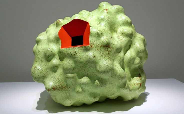 a green rock with a red house in it's center on a white surface