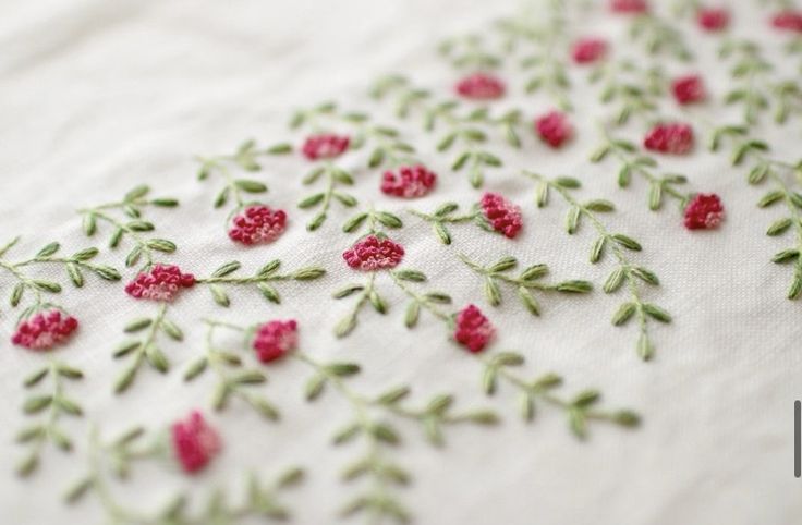 embroidered fabric with red flowers and green leaves on white linen background, closeup view