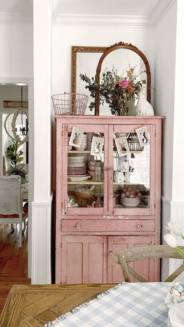 an old pink china cabinet with flowers on top in a white dining room decorated for easter