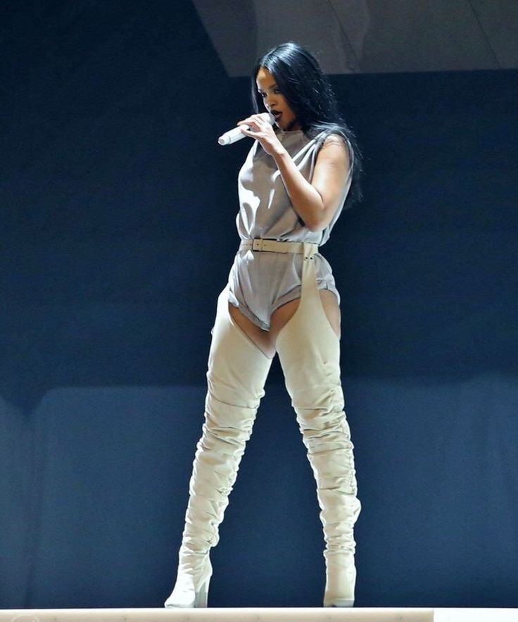 a woman standing on top of a stage wearing white pants and thigh high boots with her hands in her pockets