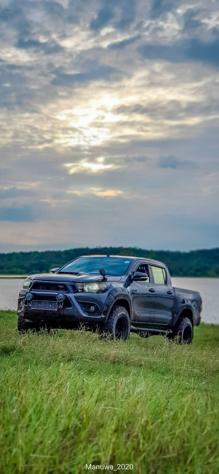 two pickup trucks parked next to each other in the grass near a body of water