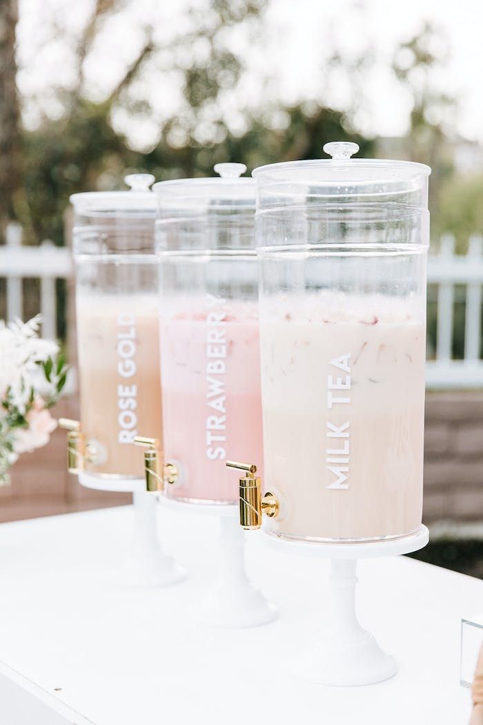 three drinks in plastic containers sitting on top of a white table next to a vase with flowers