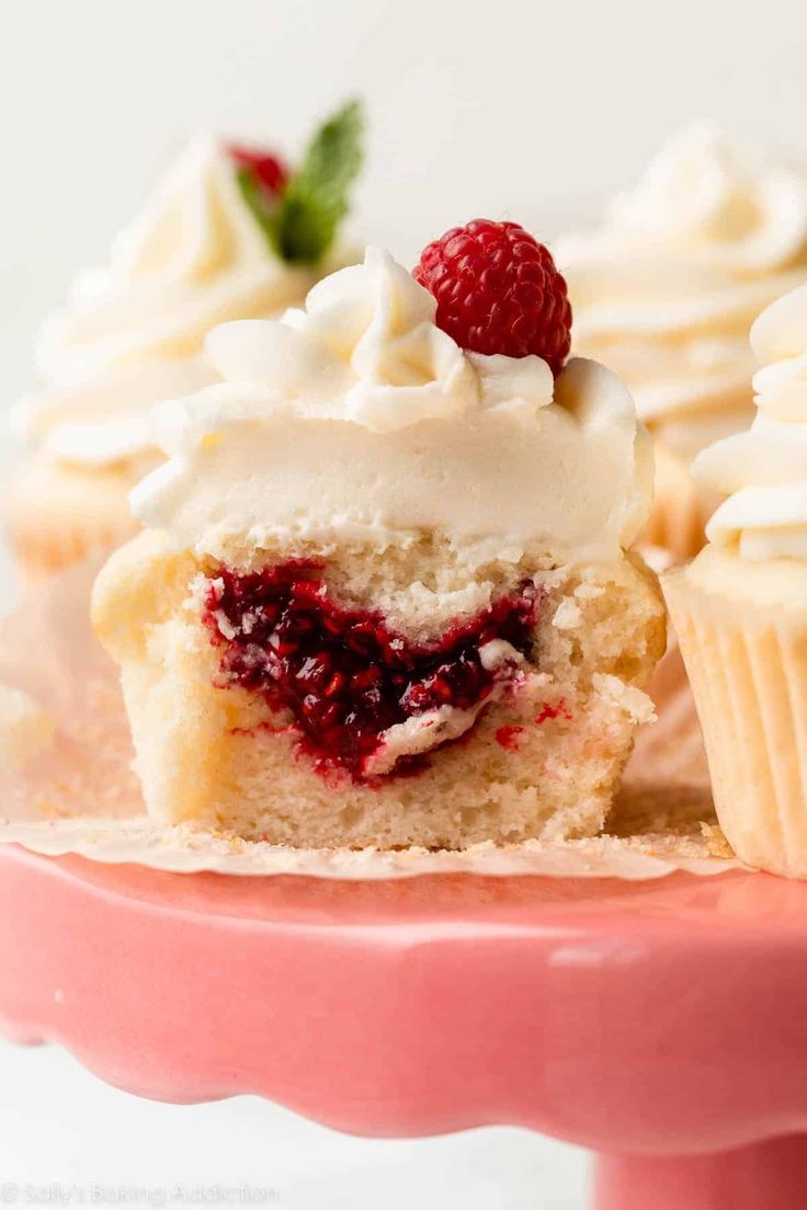 two cupcakes with white frosting and raspberries on top