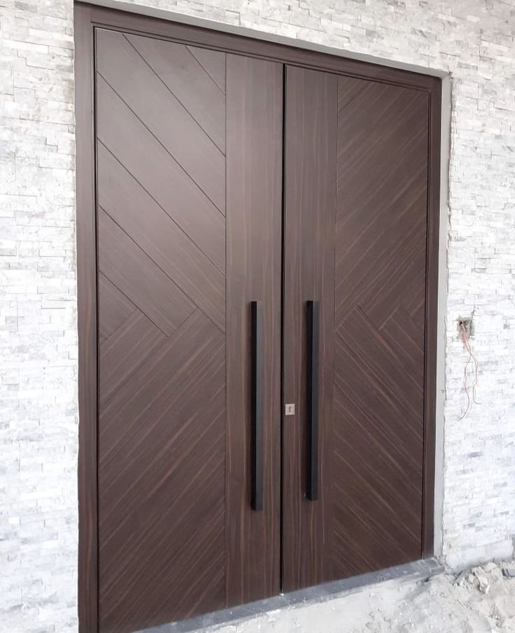 two brown doors with black handles on brick wall