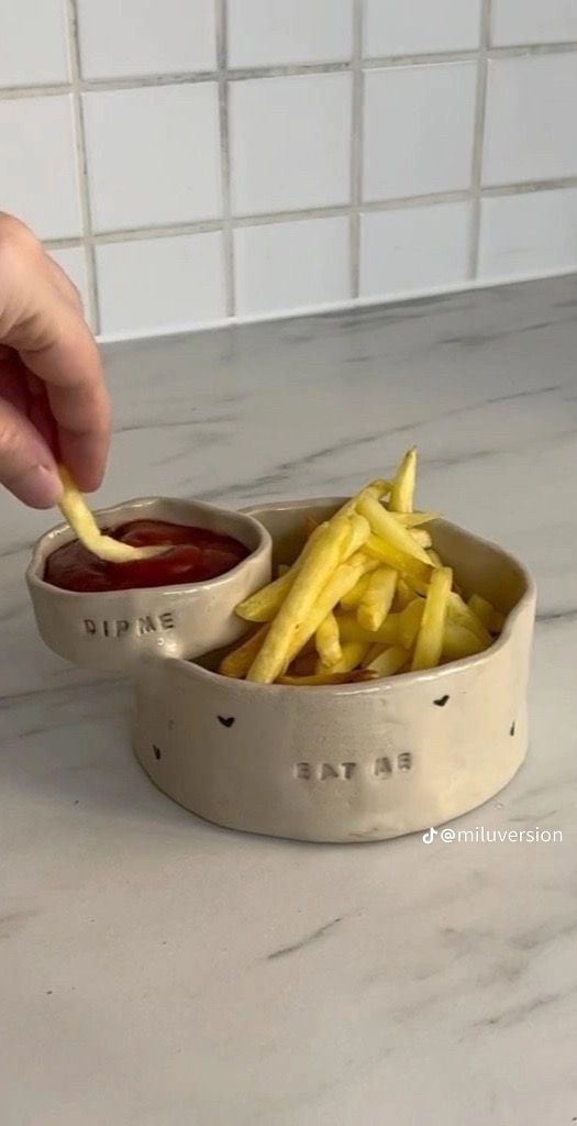 a person dipping french fries into a bowl with ketchup on the side,