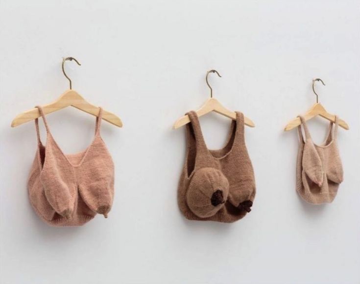 three baby bibs hanging from clothes hangers on a white wall, one is brown and the other is pink