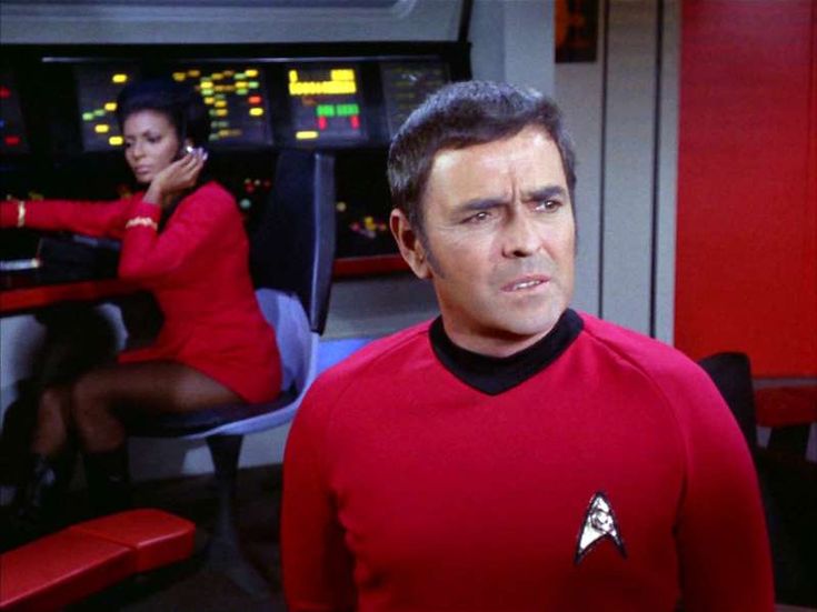 a man in a red uniform standing next to another man wearing a star trek shirt