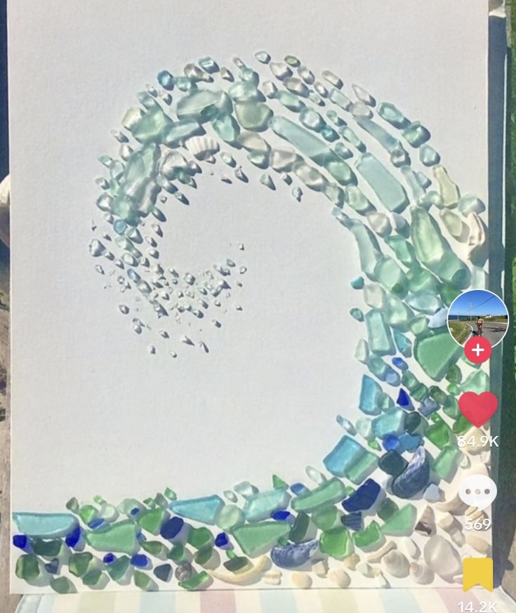 a white card with blue and green glass beads on it, in the shape of a letter o