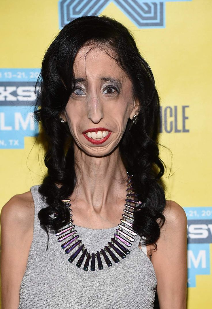 a woman with black hair and blue eyes wearing a gray top is posing for the camera