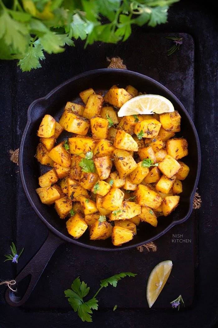 a pan filled with cooked potatoes and garnished with cilantro, parsley and lemon wedges