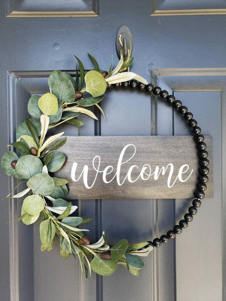 a wreath with the word welcome hanging on it's front door, next to a black beaded bracelet