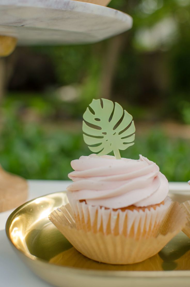 cupcakes with pink frosting and green leaves are on a gold platter