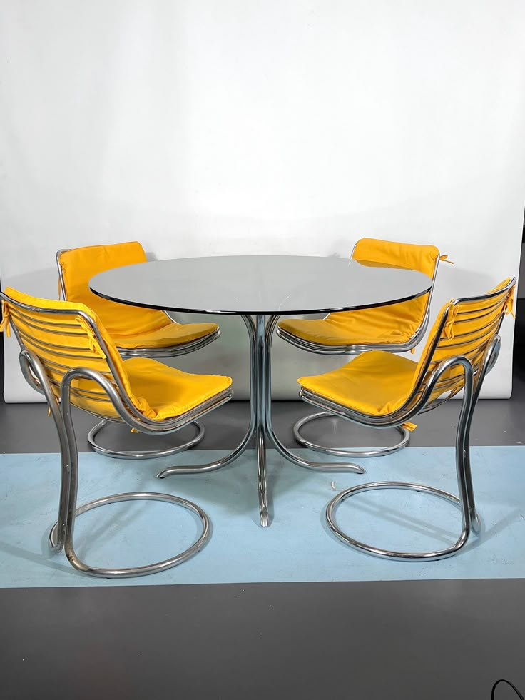 a glass table with four yellow chairs in front of a white wall and black floor