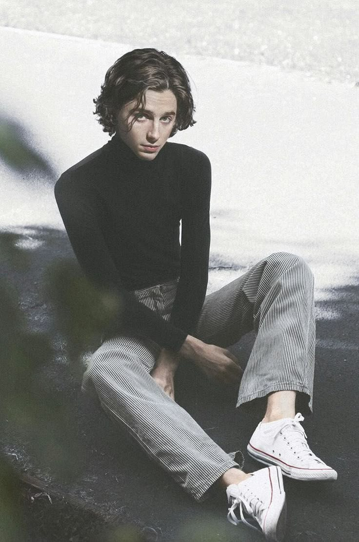 a young man sitting on the ground with his legs crossed and wearing white tennis shoes