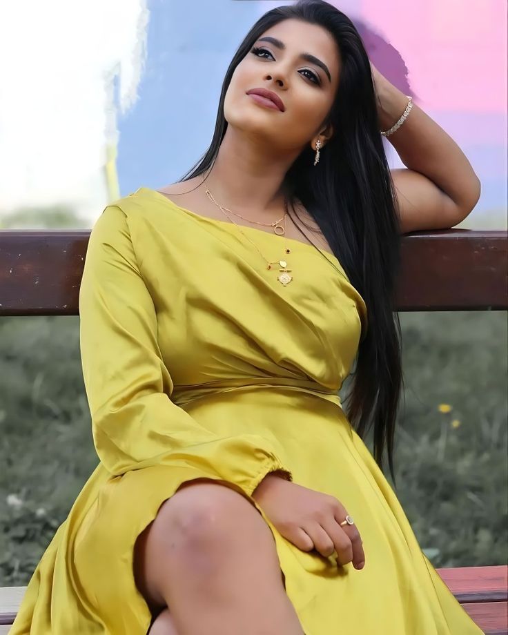 a woman in a yellow dress is sitting on a bench and posing for the camera