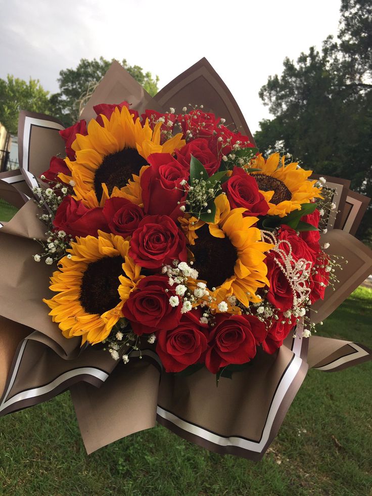 a bouquet of sunflowers and red roses on display in the grass at a park