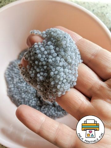 a hand holding a tiny gray object in a bowl on top of a carpeted floor