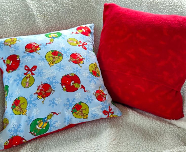 two red and blue pillows sitting on top of a white bed next to each other