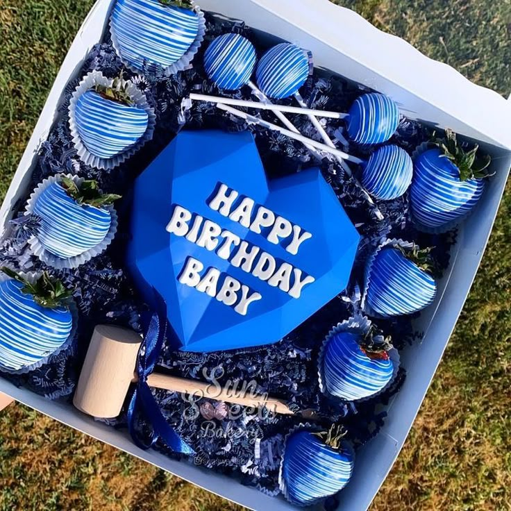 a blue birthday box filled with cupcakes and baseball bats on top of grass